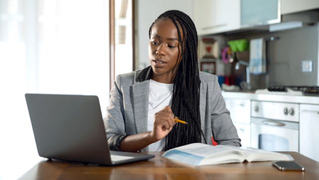 Online instructor in front of laptop referencing textbook