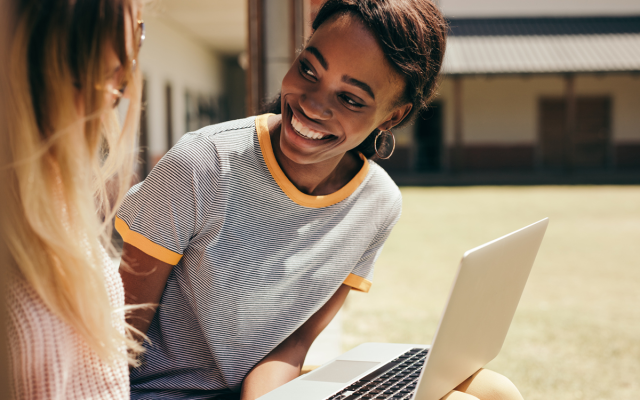 High school student working on laptop and talking to friend
