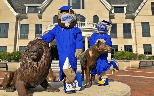 Chester and Melrose mascots in blue caps and gowns standing at Pride statues