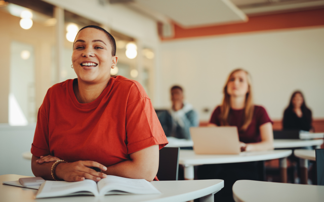 Adult student in a classroom setting smiling while wearing an orange shirt