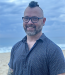 Justin Sitron wearing a blue shirt smiling at the camera on the beach
