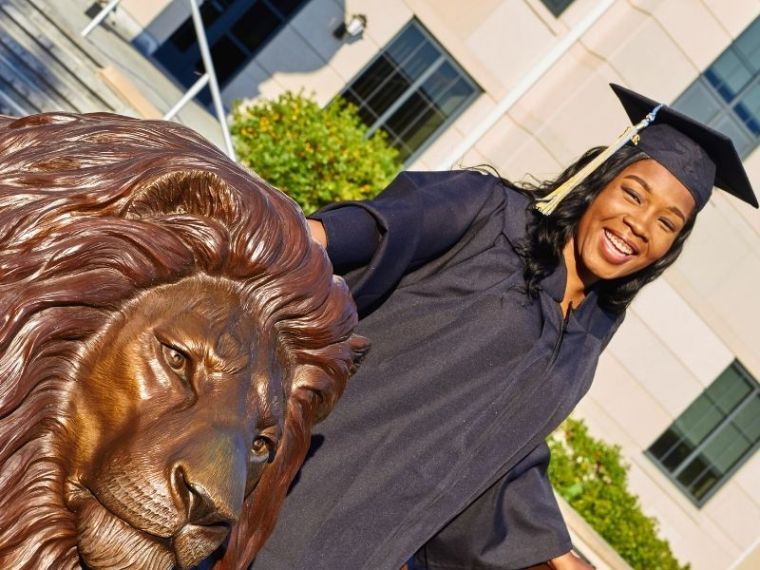 A graduate poses at the Pride statue in her cap and gown.