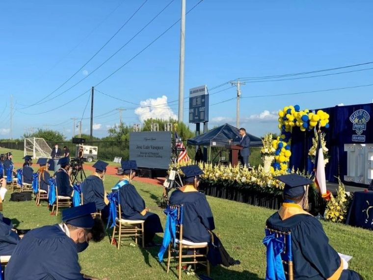 Jose-Luis Vasquez stands on platform in front of high school graduates in caps and gowns