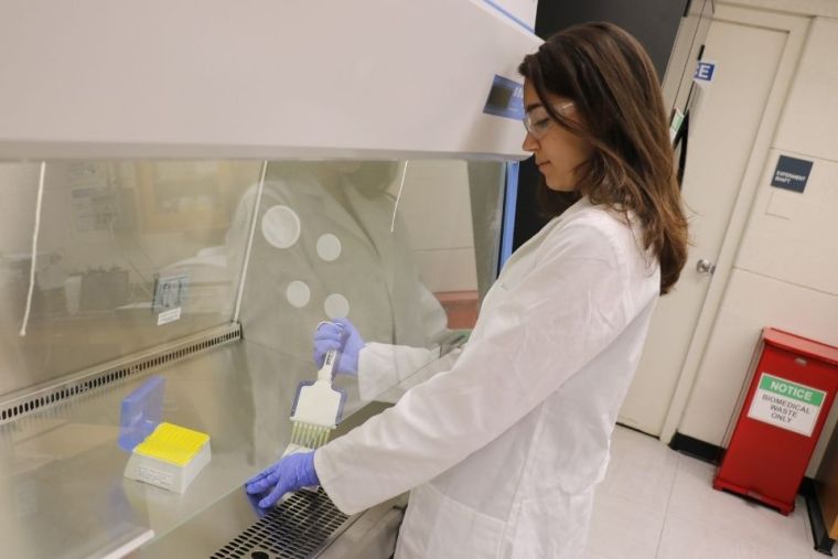 Female student in a lab coat with goggles on conducting research