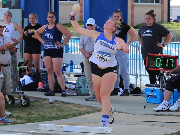Anna Cooney throws a shot put at nationals while wearing a Widener shirt, as other competitors look on