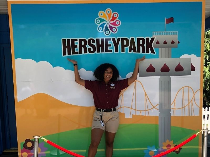 Donya Moore stands in front of a Hershey Park sign with her hands in the air