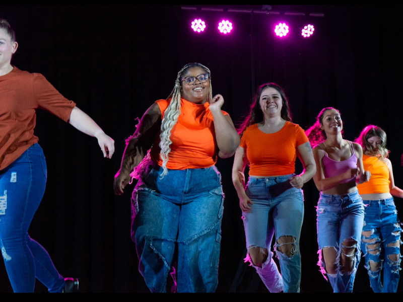 Ivana and members of the Widener Dance Company perform wearing blue jeans and orange tops
