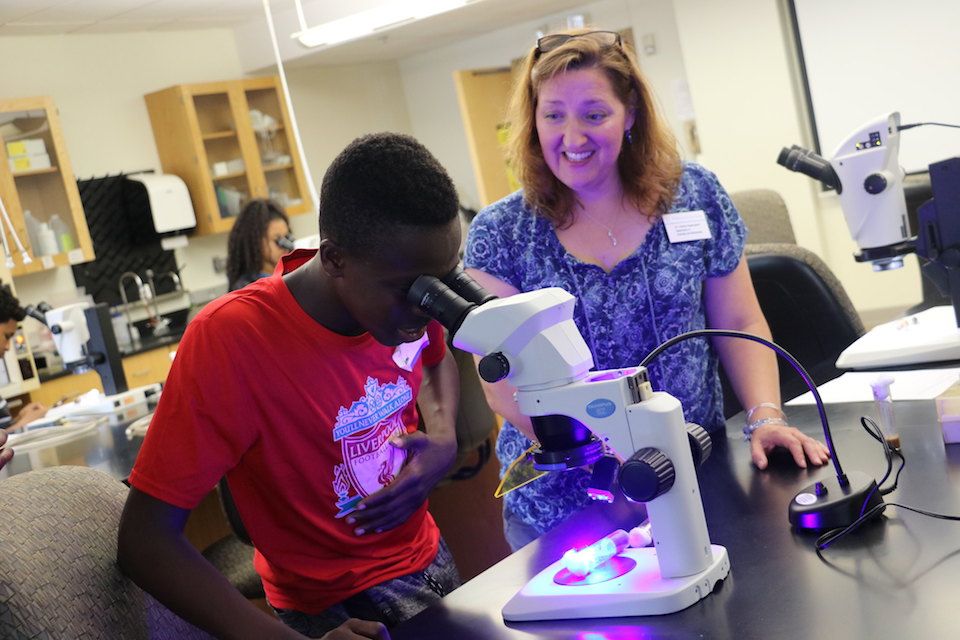 Science student looking into microscope with professor